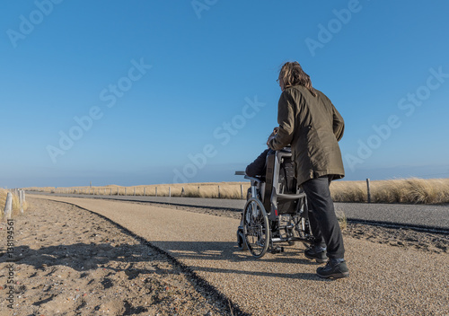 Working together with disability / A womand pushing a wheelchair with a disabled child along a gravel footpath on a bright sunny day