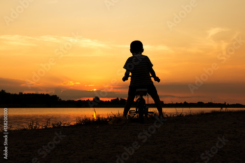 Cute little boy play and riding bicycle sunset background