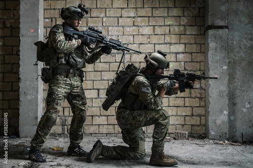 Pair of US Army Rangers with machinegun and rifle moving along the wall after each other on military mission