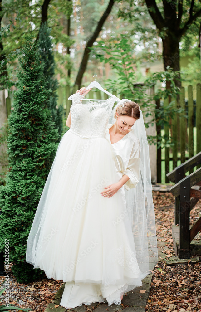 Bride in silk robe tries on wedding dres standing on porch covered with fallen leaves Bride in silk robe tries on wedding dres standing on porch covered with fallen leaves