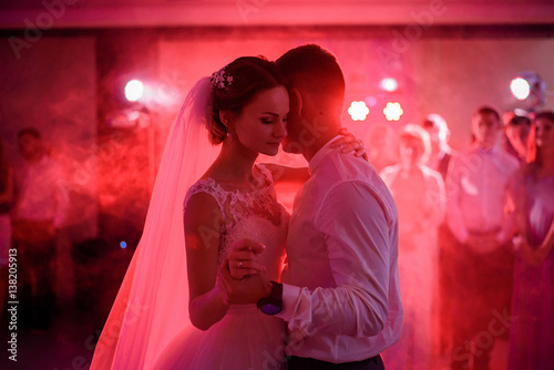 Bride and groom hug each other tender dancing in red disco lights