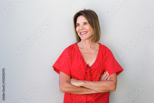 older woman smiling against gray wall with arms crossed