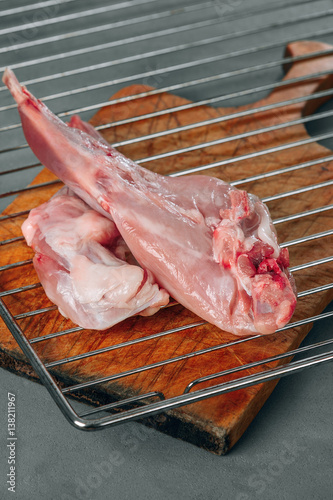Preparation of rabbit meat raw. On the table on a gray background are two animal paws. It emerges on the surface blood visible rabbit muscle and bone. 