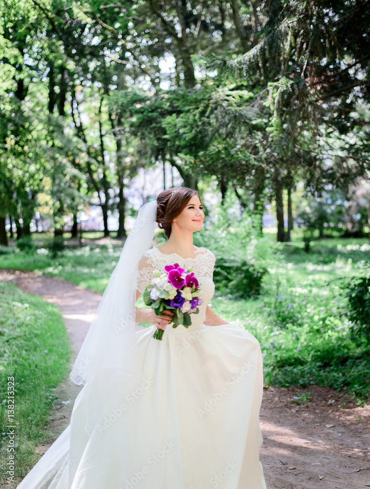 Bride holds her magnificent dress walking in it around green park