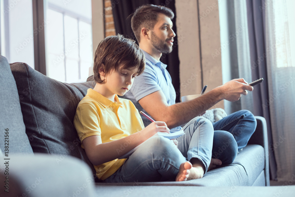 father watching movie and eating breakfast while son doing homework father watching movie and eating breakfast while son doing homework