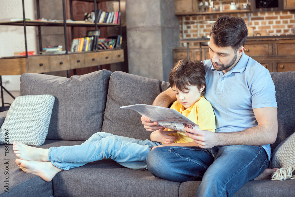 focused father and son reading newspaper together at home