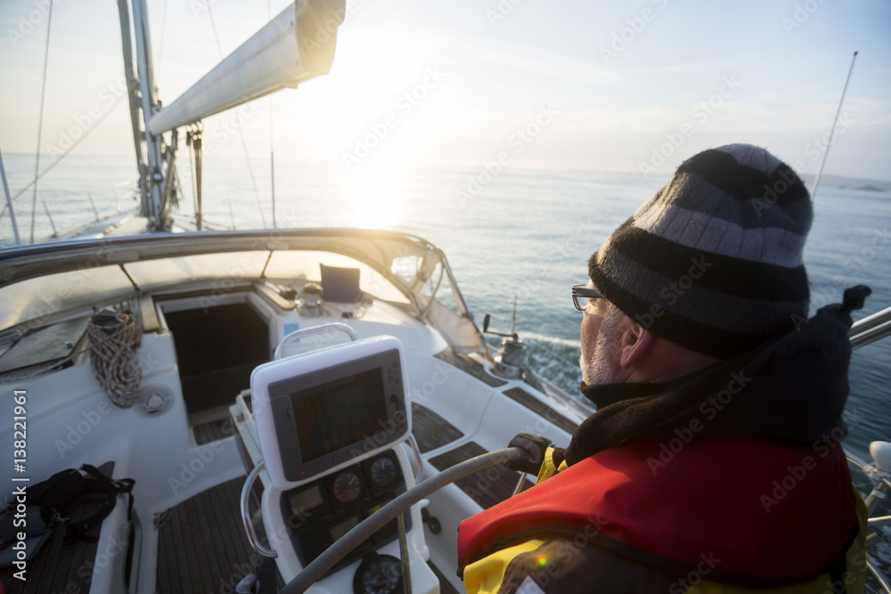 Fototapeta premium Man Steering Yacht At Helm During Sunset