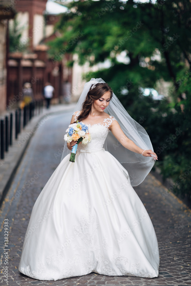The beautiful bride keeps a bouquet and walks along street The beautiful bride keeps a bouquet and walks along street