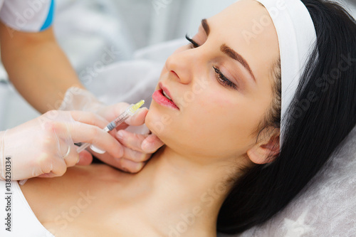 Hands of cosmetologist making injection in face, lips. Young woman gets beauty facial injections in salon. Face aging, rejuvenation and hydration procedures. Aesthetic cosmetology. Close up. photo