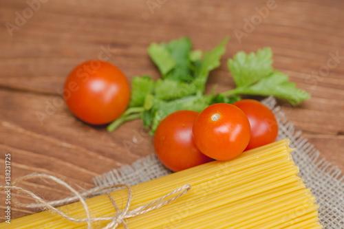 На столе лежат спагетти с помидорами и зеленью.