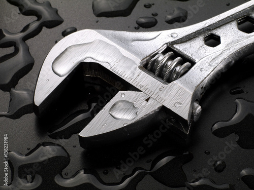 adjustable wrench on wet black background with water drops, macro