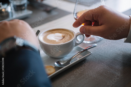 Man's hand holding a white cup of coffee with milk