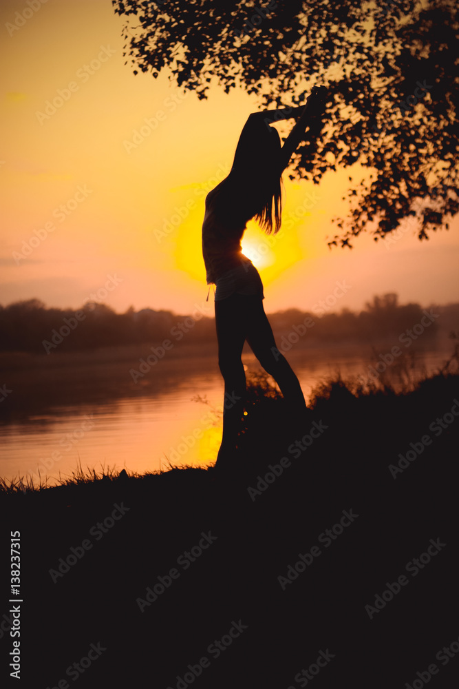 Silhouette of dancing girl at sunset by the lake