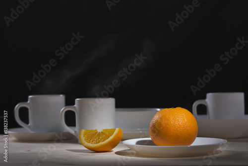 White mug with the steam from the tea next to a slice of orange on a black background