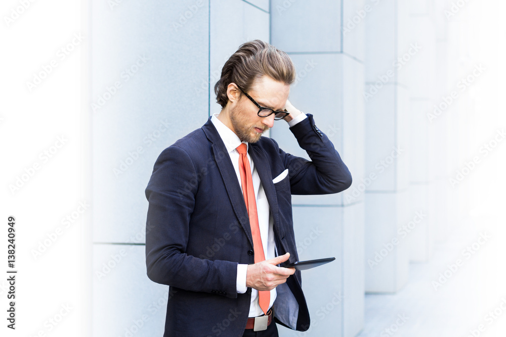Bearded businessman in glasses looking at the tablet, puzzled. Space for text. Bearded businessman in glasses looking at the tablet, puzzled. Space for text.