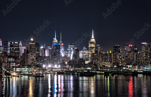 New York city skyline at night with building lights reflected in Hudson River