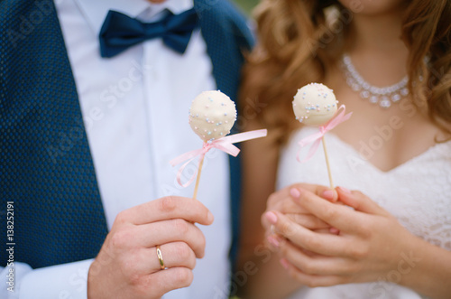 Hands of the groom in a blue suit and bow tie and the bride with cake Pops close-up