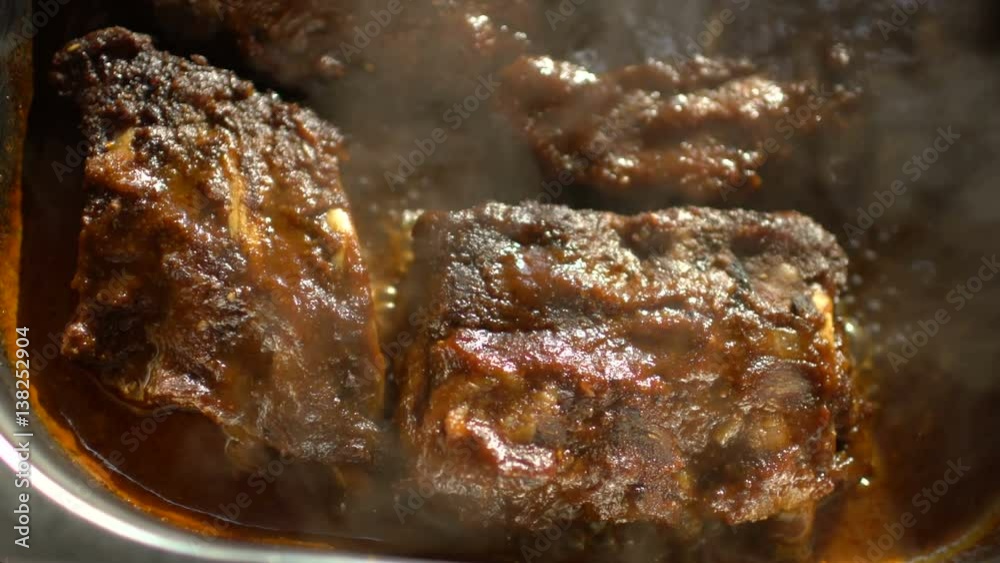 Rotating of hot meat dishes with pork ribs with gravy boiling sauce at restaurant kitchen Rotating of hot meat dishes with pork ribs with gravy boiling sauce at restaurant kitchen