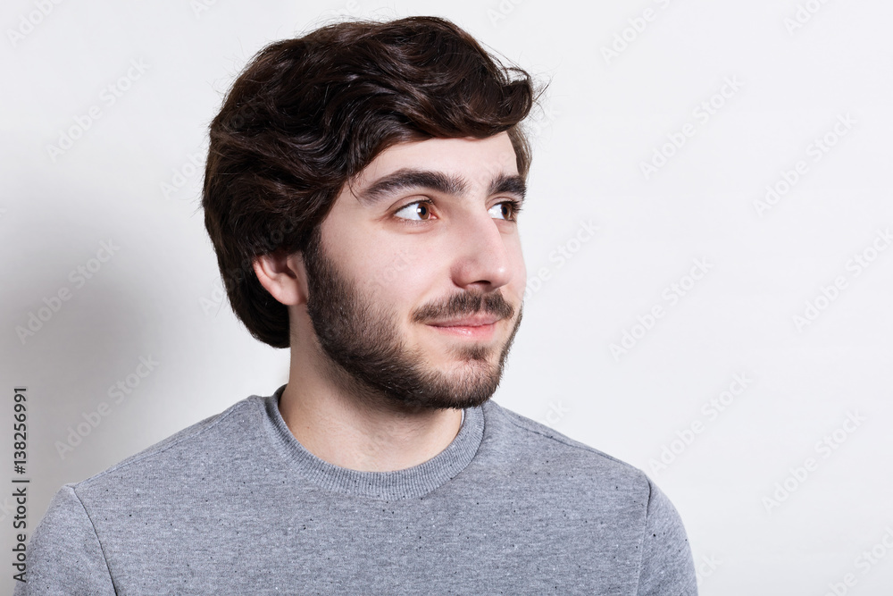A close-up of stylish hipster with trendy beard and hairstyle, dark big eyes dressed in casual clothes looking happily aside. Portrait of handsome man with beard over white background A close-up of stylish hipster with trendy beard and hairstyle, dark big eyes dressed in casual clothes looking happily aside. Portrait of handsome man with beard over white background