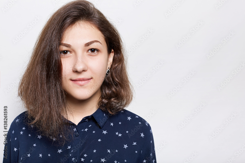 Half profile of young attractive female with dark charming eyes and with fashionable haircut, dressed in stylish shirt wearing black elegant earrings looking directly into camera. Half profile of young attractive female with dark charming eyes and with fashionable haircut, dressed in stylish shirt wearing black elegant earrings looking directly into camera.