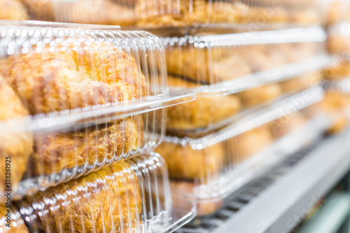 Billede på lærred Many plain croissants packaged in plastic boxes on display in store