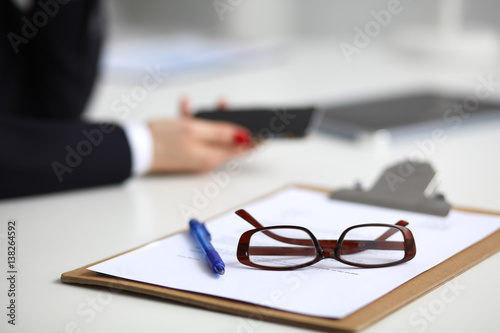 Businesswoman using her phone in office sitting on desk