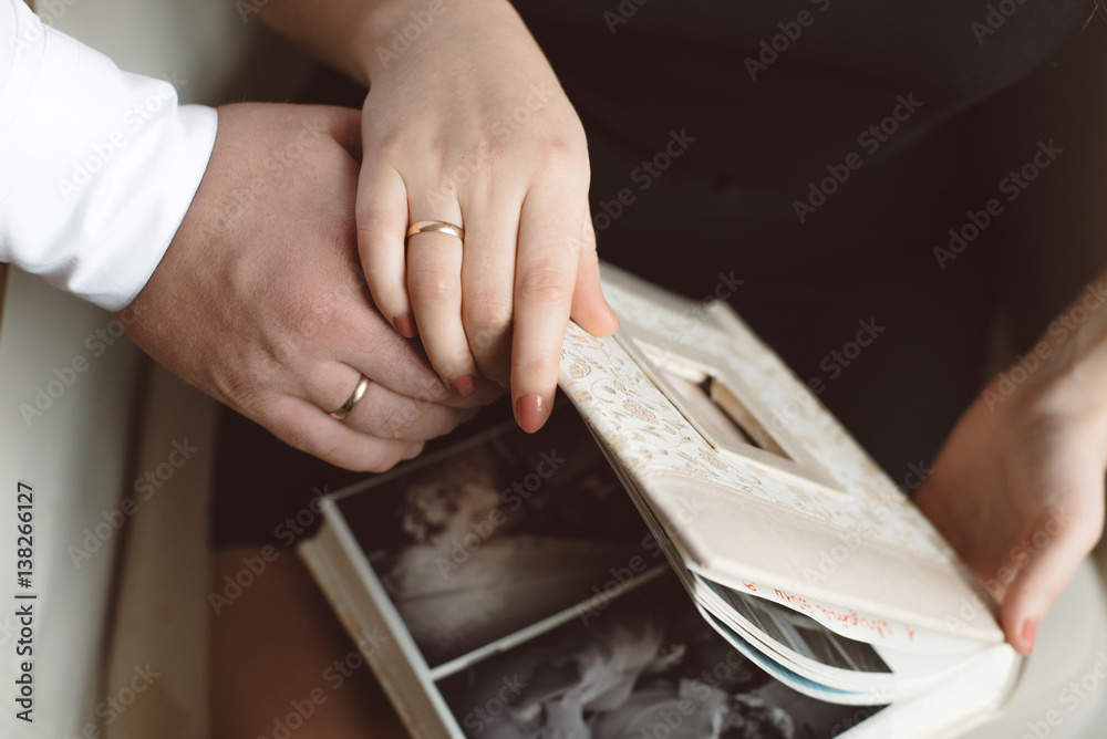 Man and woman watching a photo album beige close-up of hands in wedding rings