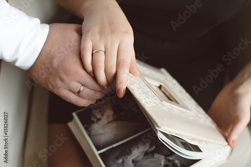 Man and woman watching a photo album beige close-up of hands in wedding rings