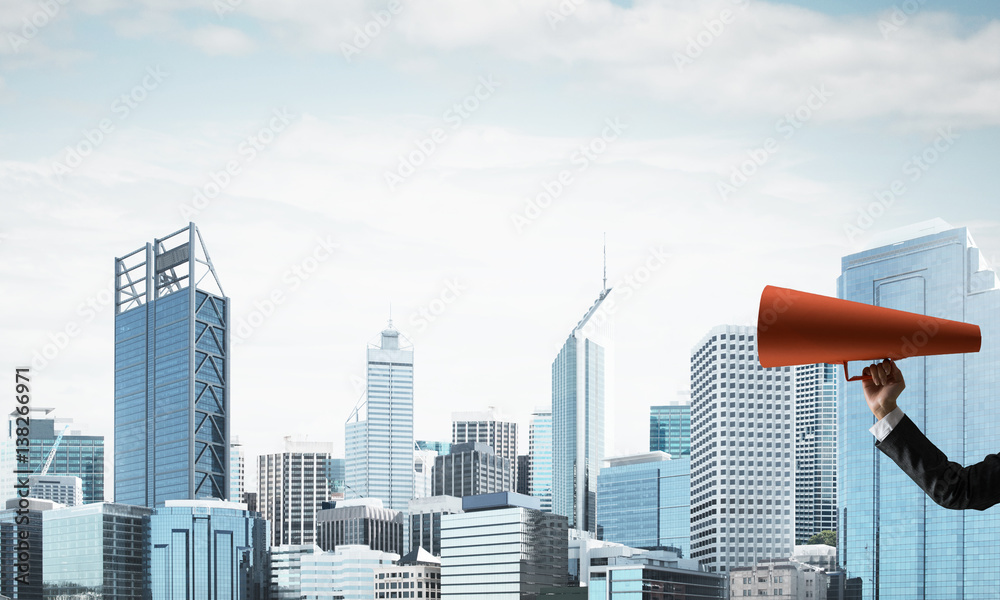 Hand of businesswoman holding red paper trumpet against cityscape background
