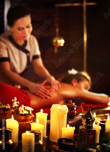 Massage of woman in spa salon. Girl on candles background treats problem back spa salon. Luxary interior with working masseuse . Shirodhara Pot background. Female bare back has relax .