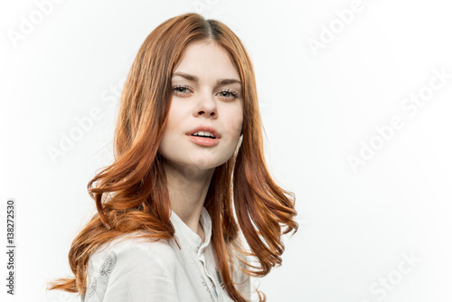 red-haired woman on a light background looks at the camera
