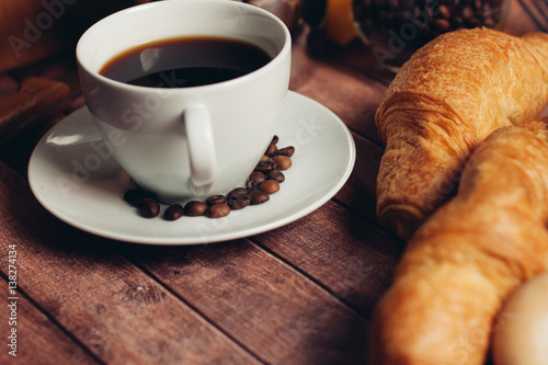 coffee beans in a saucer, a cup with a drink and two croissants