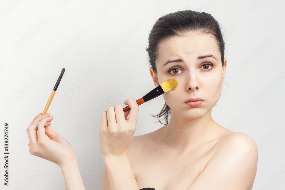 brunette with a sad expression on her face holding two makeup brushes brunette with a sad expression on her face holding two makeup brushes