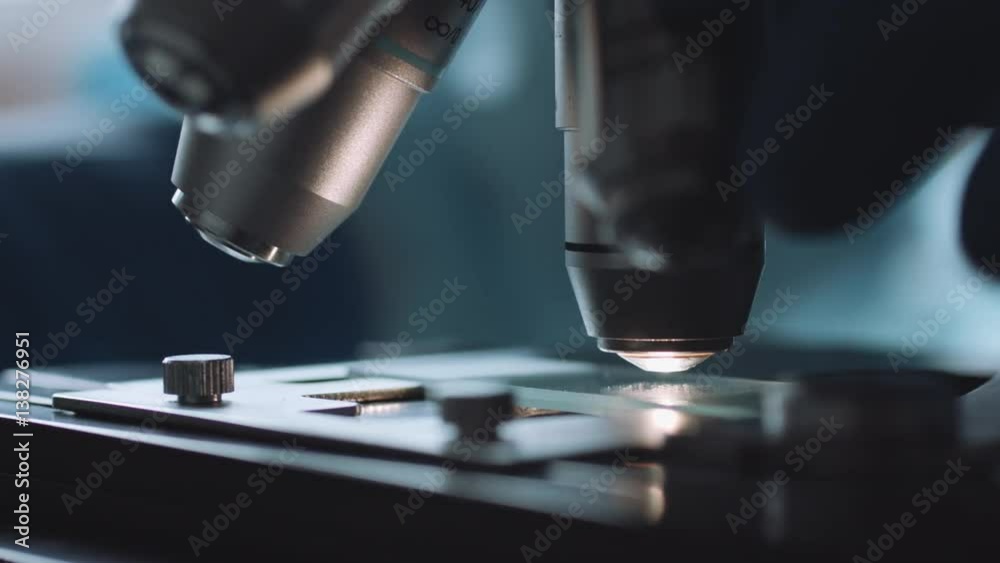 Close up view of scientist hands with gloves set the sample in the microscope for research