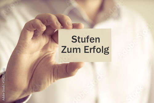 Businessman holding message card Stufen Zum Erfolg written in German - translation : Steps To Success