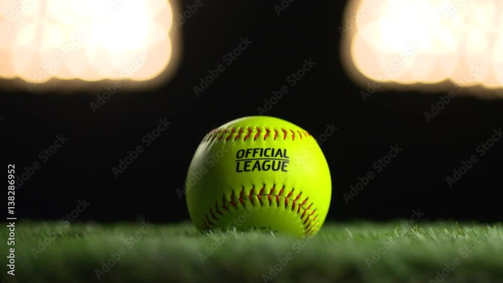 A softball spins under the stadium lights.