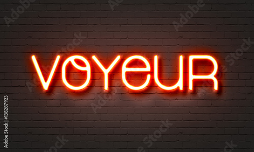 Voyeur neon sign on brick wall background. photo