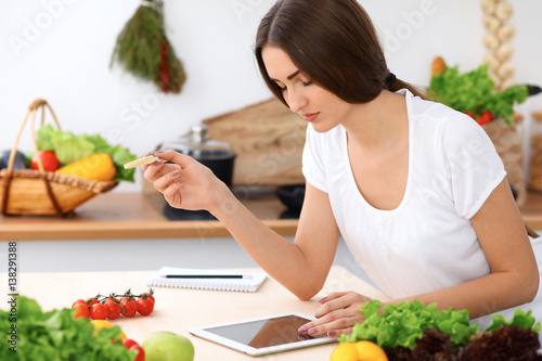 Beautiful Hispanic woman is making online shopping by tablet computer and credit card or searching internet for a new recipe. What to cook for a dinner?