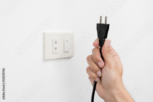 Hand of man unplug electric outlet plug on wall white background safety concept photo