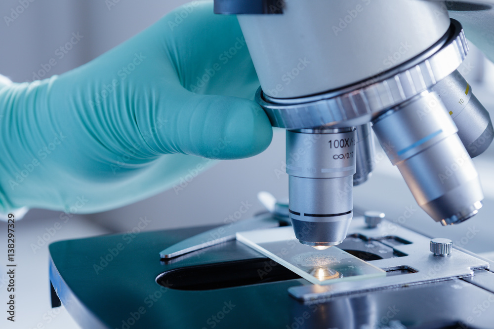 Close up view of scientist hands with gloves set the sample in the microscope for research Close up view of scientist hands with gloves set the sample in the microscope for research