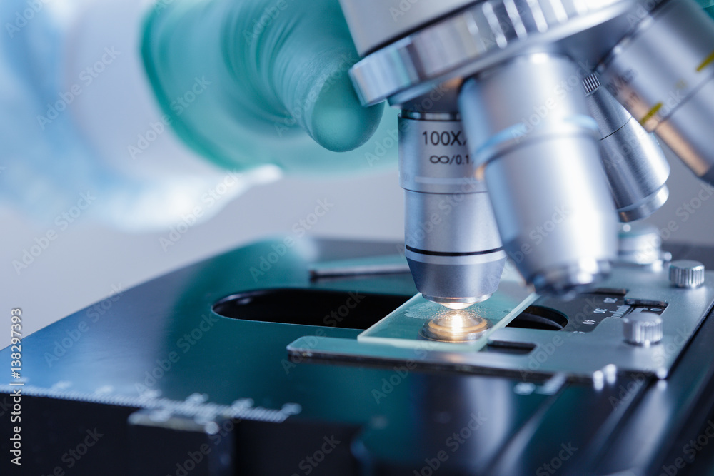 Close up view of scientist hands with gloves set the sample in the microscope for research