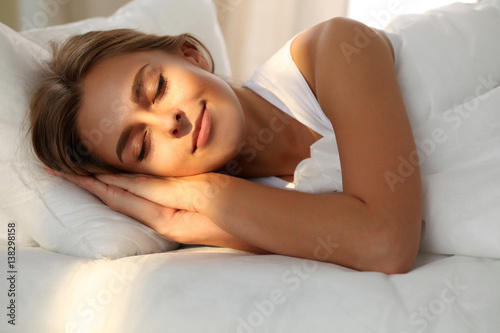 Beautiful young woman sleeping while lying in bed comfortably and blissfully. Sunbeam dawn  on her face