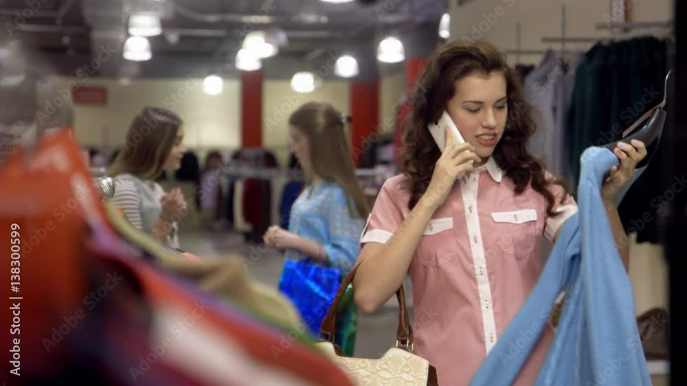 Young brunette girl is shopping for dresses while speaking on the phone in a department store. Young brunette girl is shopping for dresses while speaking on the phone in a department store.