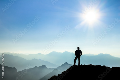 Man reaching summit enjoying freedom and watching towards mountain ranges.