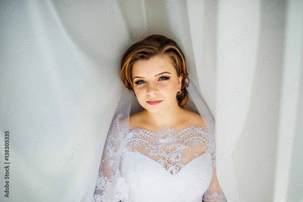 Cute blonde bride posed on curtains at wedding morning day. Cute blonde bride posed on curtains at wedding morning day.