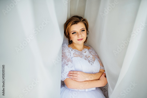 Free Download Cute blonde bride posed on curtains at wedding morning day. - GFXLoad