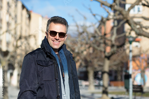Handsome happy smiling man. Outdoor winter male portrait. Attractive confident middle-aged man in sunglasses walking in city.