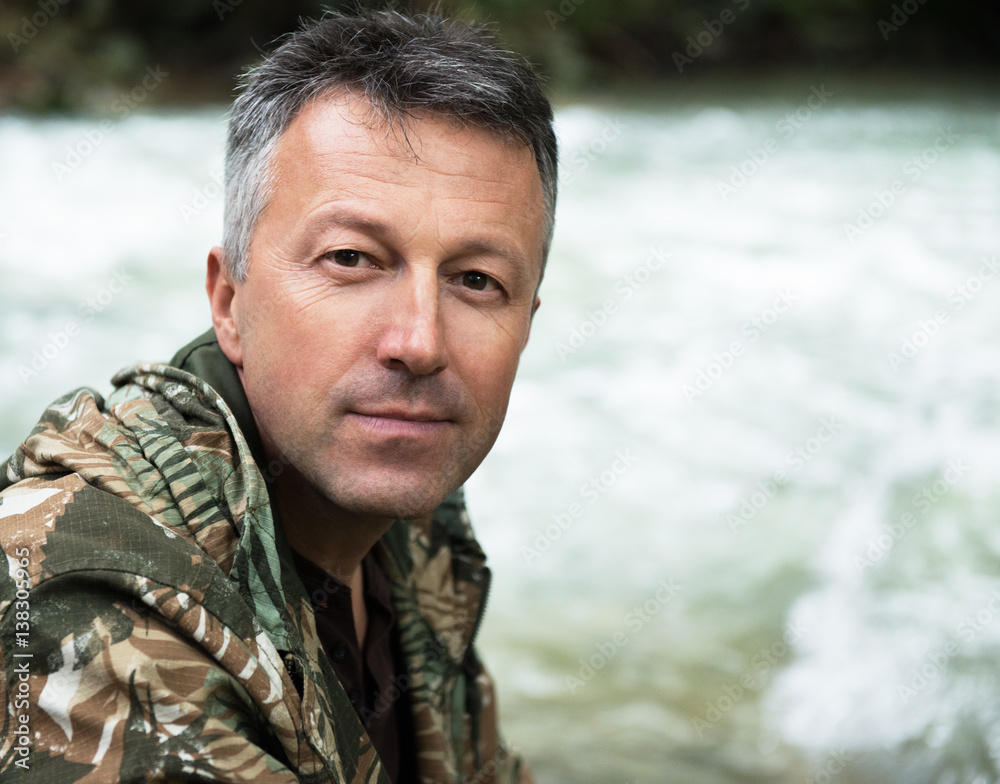 Outdoor autumn male portrait. Man sitting on rocks near mountain river, image toned and noise added. Outdoor autumn male portrait. Man sitting on rocks near mountain river, image toned and noise added.