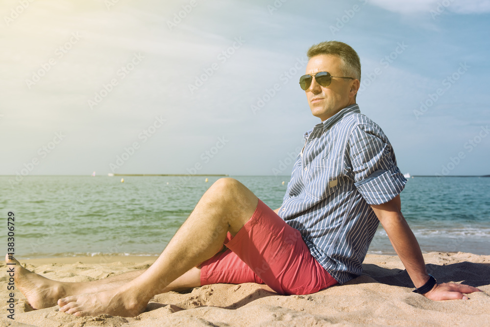 Man is sunbathing on sea coast, summer nature outdoor. Portrait of handsome middle-aged man rests on the beach, image toned.