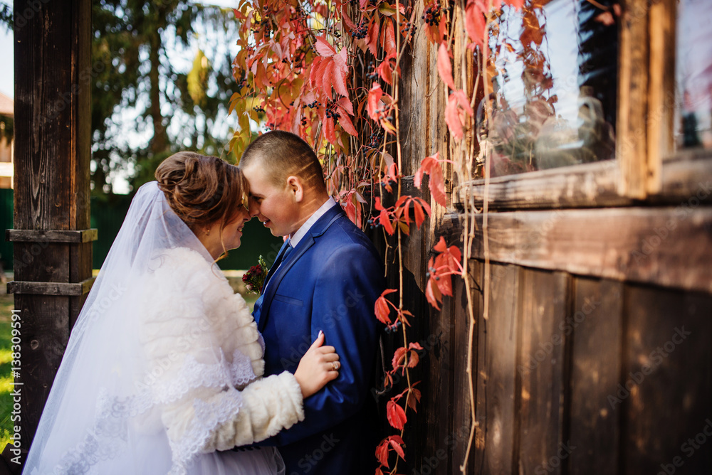 Wedding couple against old wooden house with red leaves on his. Wedding couple against old wooden house with red leaves on his.